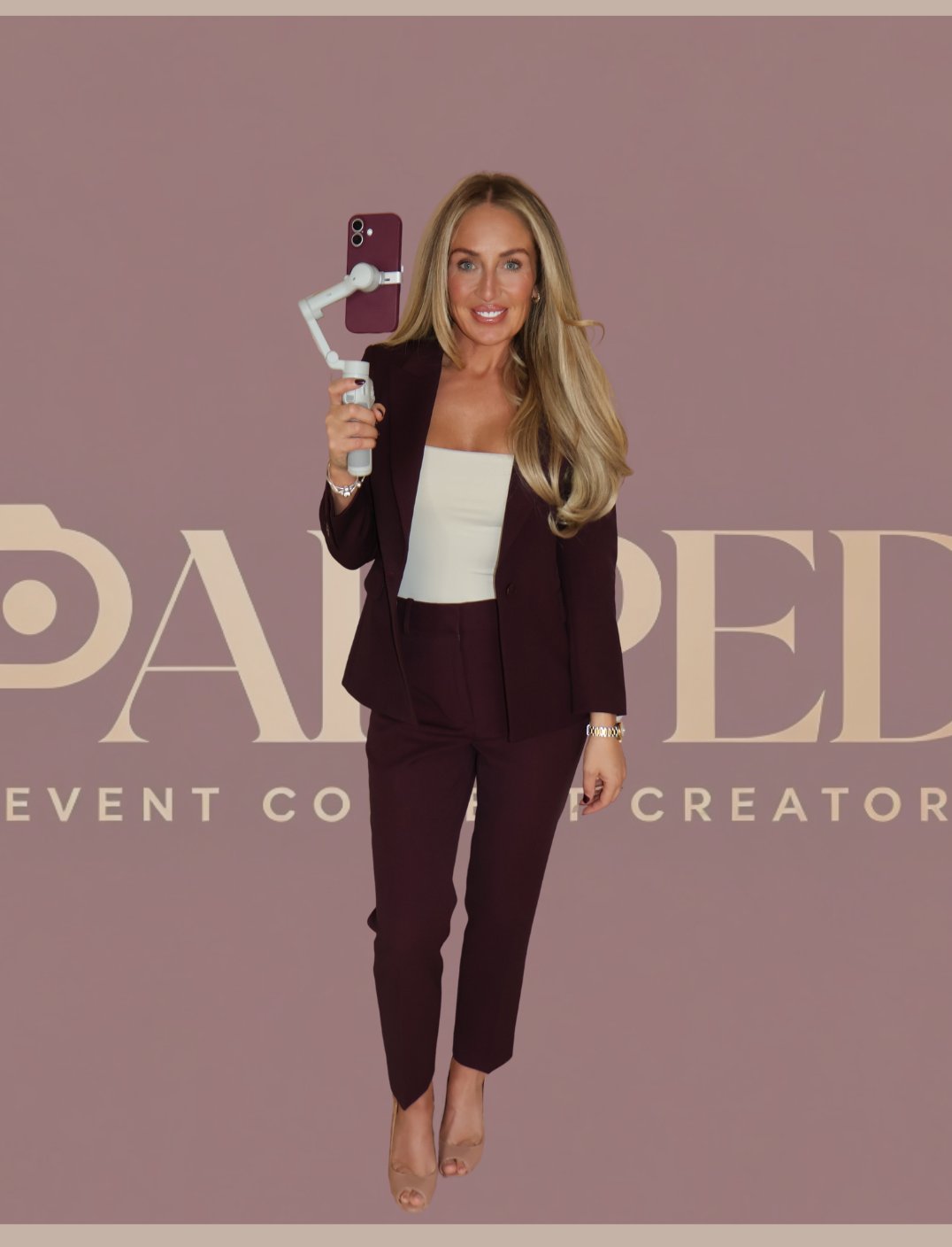 Chelsea, founder of PAPPED, in a plum suit holding a phone on a gimbal and smiling in front of the PAPPED logo